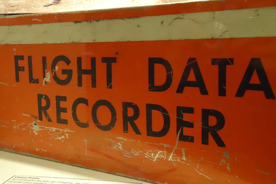 An orange flight data recorder on display, with the words Flight Data Recorder painted on its side