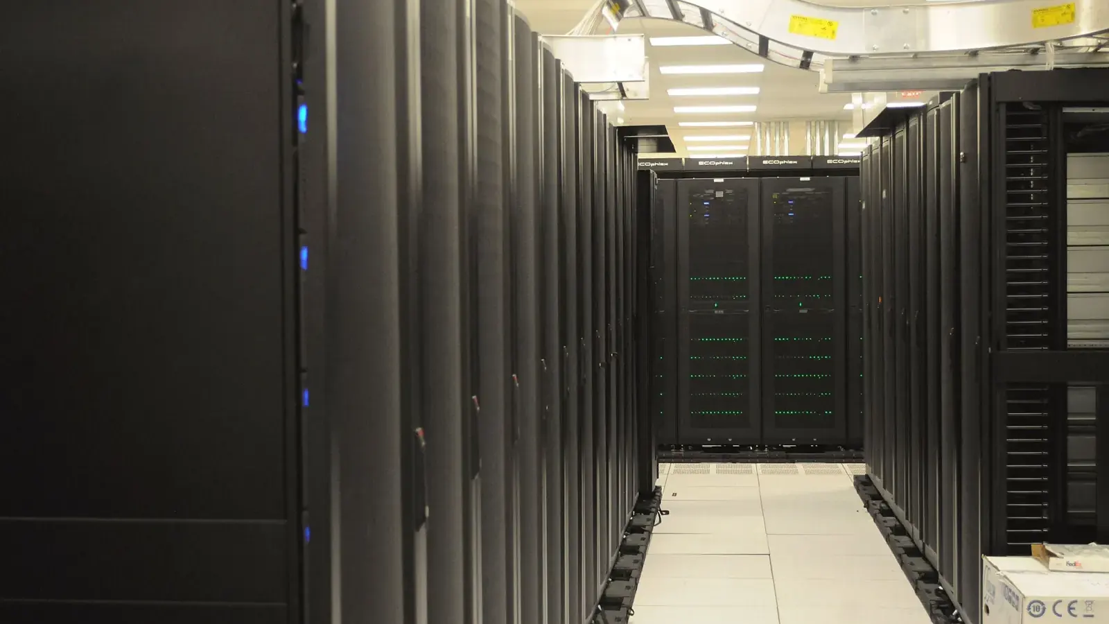 Aisle between two rows of black server racks with small status lights in a supercomputing centre