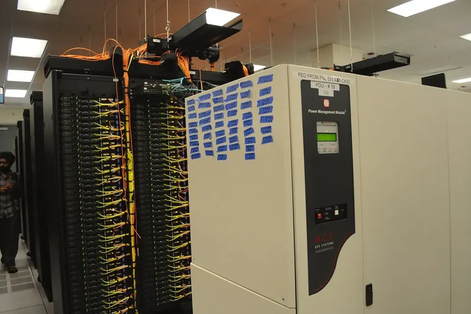 Server racks with bundles of yellow network cables next to a power distribution cabinet in a data centre