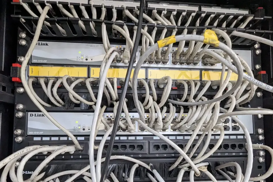 A tangle of grey network cables hanging in front of patch panels and switches in a rack